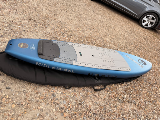 North Midi 6'4 96L wing foil board, side rail profile resting on its Mystic padded board bag