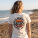 Woman wearing Boardworx Surf Shop Natural Raw V-neck T-shirt on Whitstable beach, back logo view