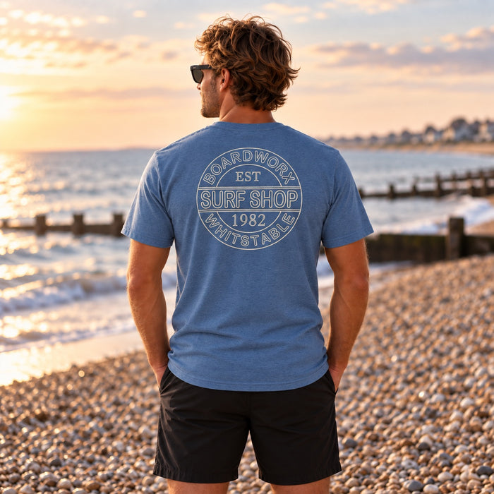 Man wearing the Boardworx Surf Shop indigo blue T-shirt on a Whitstable shingle beach, back logo view