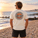 Man wearing the Boardworx Surf Shop ivory white T-shirt on a Whitstable shingle beach, back logo view