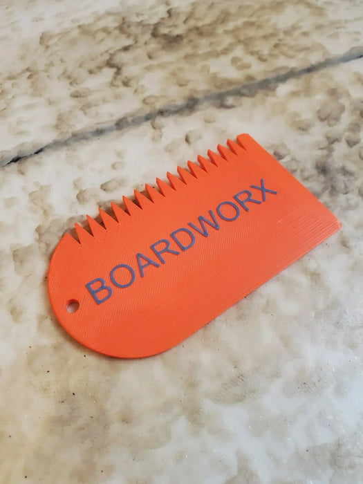 Orange BOARDWORX surf wax comb scraper on a marbled surface