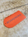 Orange BOARDWORX surf wax comb scraper on a marbled surface