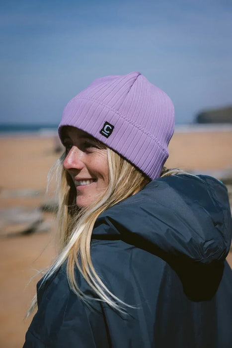 C-Skins lilac neoprene beanie for watersports, worn by woman on sandy beach