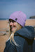 C-Skins lilac neoprene beanie for watersports, worn by woman on sandy beach