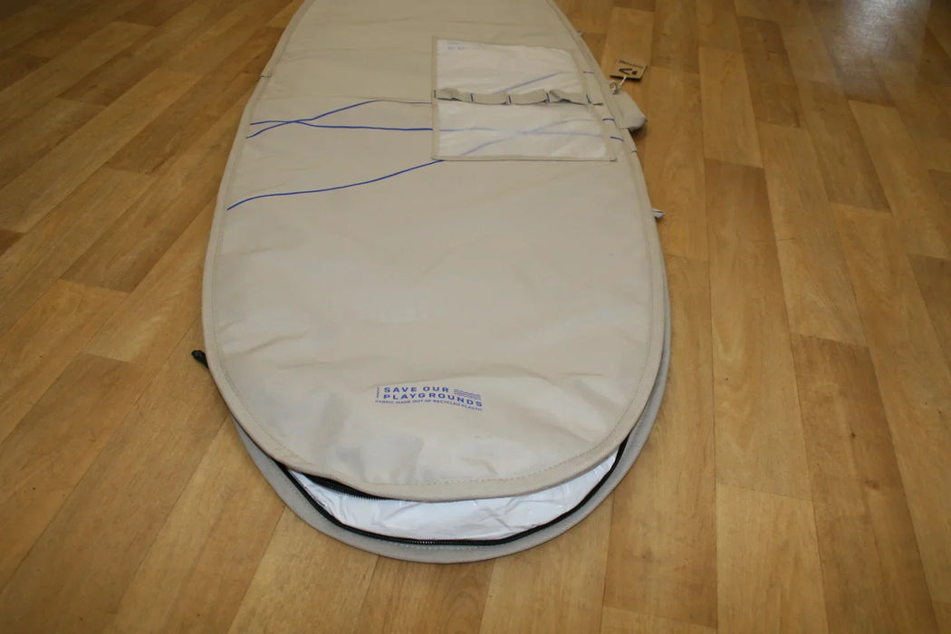 Duotone beige surfboard bag 6ft with blue accents and exterior storage pocket on wood floor