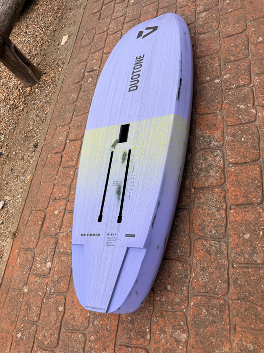 Bottom view of used Duotone Skybrid 5'10" 100L 2025 wing foil board showing foil track slots and light violet colour with yellow-green graphic
