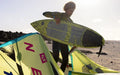 Person holding Duotone traction deck pad surfboard with yellow kite on sandy beach