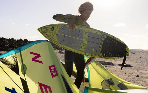 Person holding Duotone traction deck pad surfboard with yellow kite on sandy beach