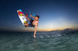 Duotone twin tip kiteboard with yellow foot straps in action, kitesurfer jumping at sunset over clear water.