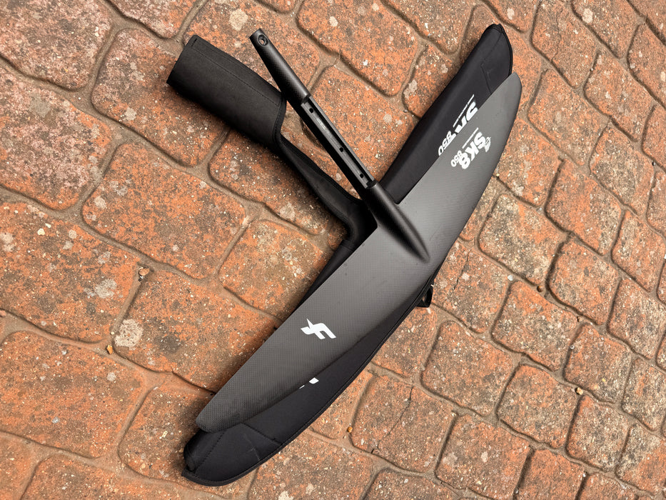 Overview of used F-one Sk8 V2 850 wing foil front wing with protective carry bag on brick paving showing F-one logo and SK8 850 bag label