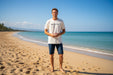 Man wearing off-white Mystic brand t-shirt and denim shorts on sandy beach by the sea