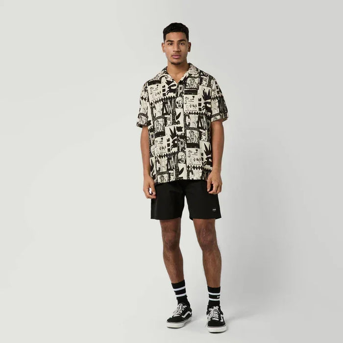 Man wearing sand and black patterned surf shirt with black shorts and trainers