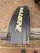 Naish Monarch black kitesurfing kiteboard with yellow graphics on pebbled ground