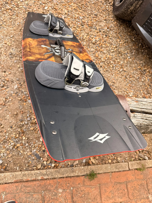 Naish Monarch kitesurfing board, black with grey footstraps, seen on a gravel surface