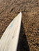 Duotone Whip D/LAB white surfboard on pebbled beach, close-up of board edge and logo
