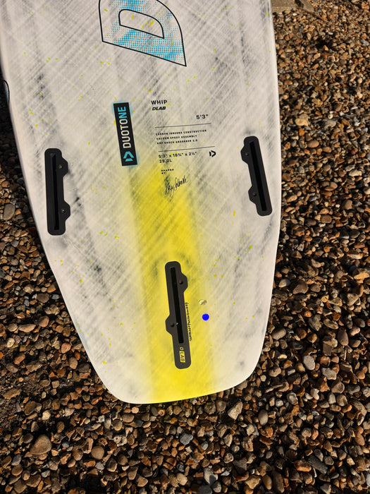 Duotone Whip DLab kite surfboard 5'3 in white with yellow accent on pebbled beach