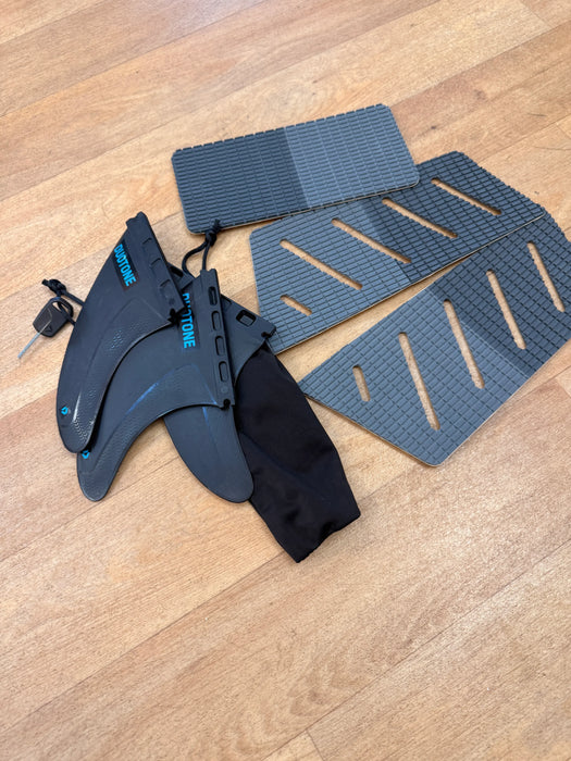 Duotone surfboard fins and grey deck pads set on a wooden floor, kite accessory kit