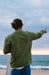 O'Neill green crew sweatshirt for surfers, back view, beach setting, surfboard in hand