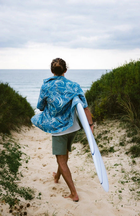 O'Neill blue UPF 50 surf shirt, person carrying surfboard on sandy path to the beach