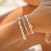 Alona Beach shell bracelet set with starfish charm, natural white beads, on wrist at beach.