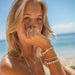 Woman wearing shell bracelet set with white beads on beach, surf style accessories