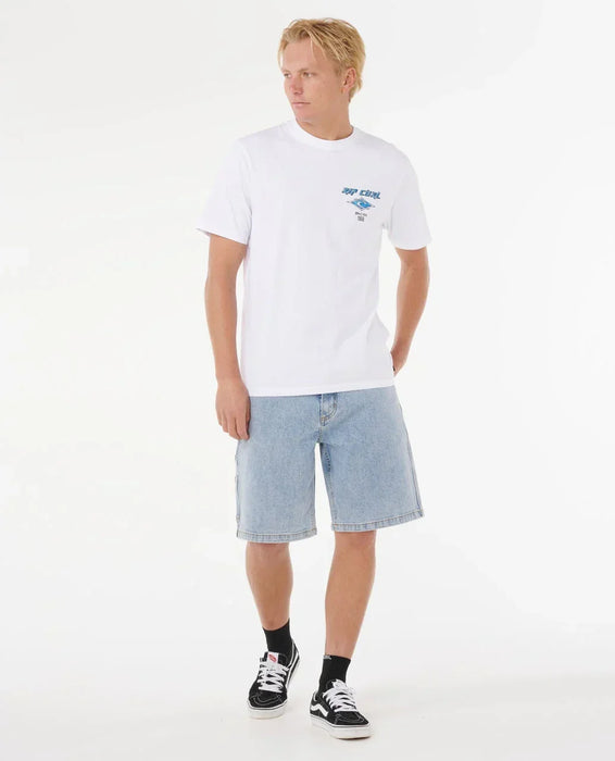 Man wearing Rip Curl white surf t-shirt with blue fade logo, denim shorts, and black trainers