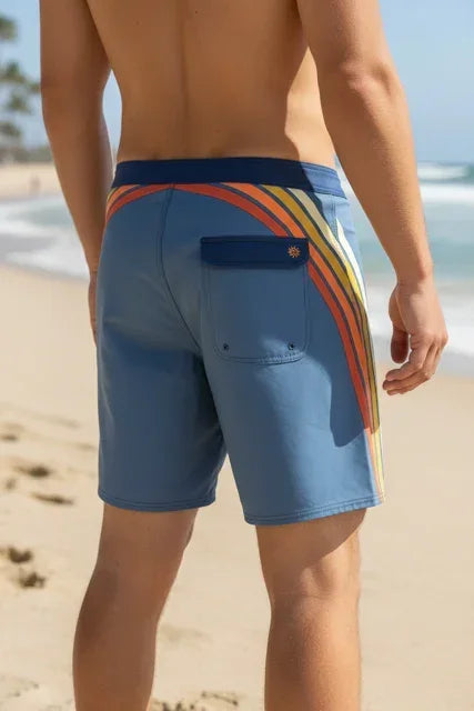 Rip Curl Mirage Pacific men's blue board shorts with rainbow stripe, beach background