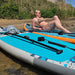 Woman relaxing on a Sandbanks Pro X Turquoise inflatable paddle board by the water