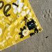 Slowtide yellow floral beach towel with white and black pattern on sand