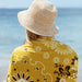 Slowtide Axel beach towel yellow floral pattern by the sea, person in straw hat