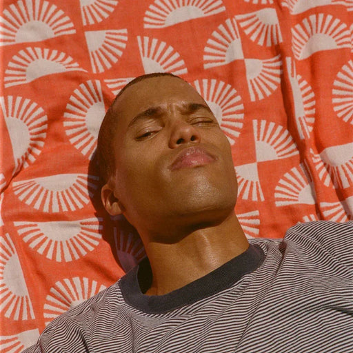Man relaxing on orange patterned beach towel, wearing striped surf shirt