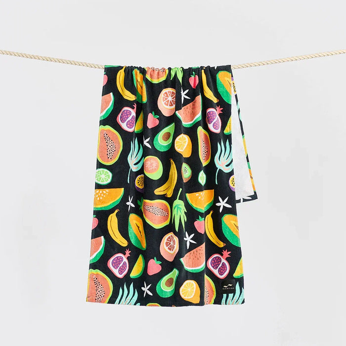 Slowtide beach towel with colorful tropical fruit print on black background, hanging on rope
